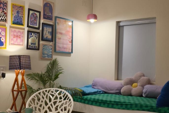 A guest room corner: a day-bed with a green mattress and cushions beneath a gallery wall of framed prints