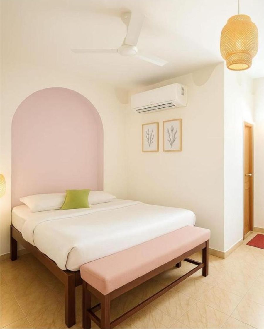 A bedroom with a pink arch behind the bed, a green cushion, a split air-conditioner, a ceiling fan and a woven pendant light