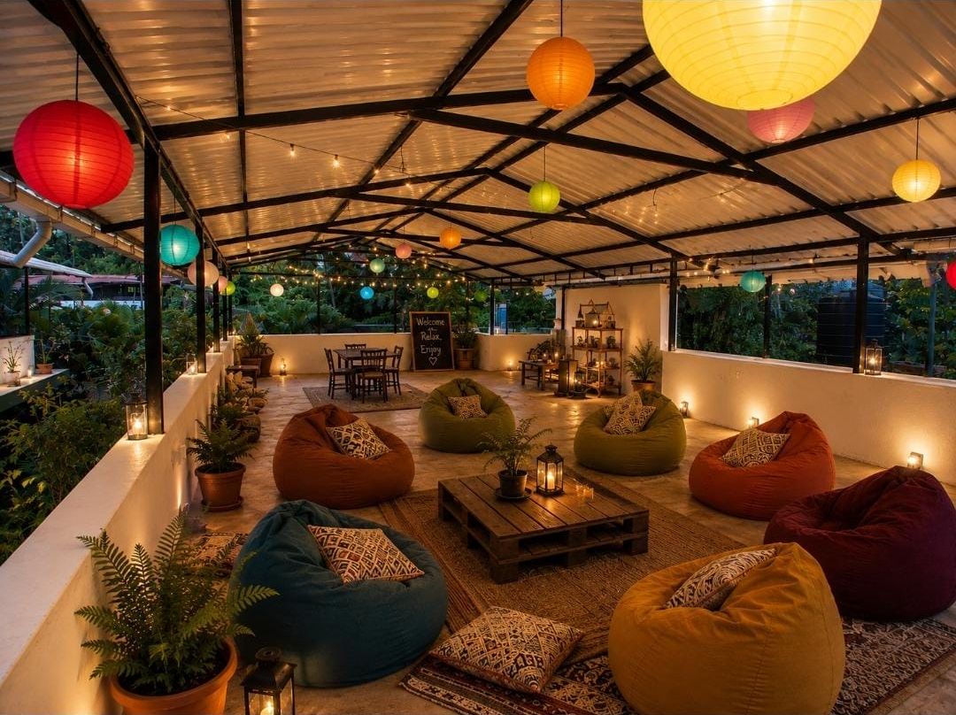 The sit-out at night: a covered terrace with bean bags round a pallet table, paper lanterns and string lights overhead, and a dining table at the back