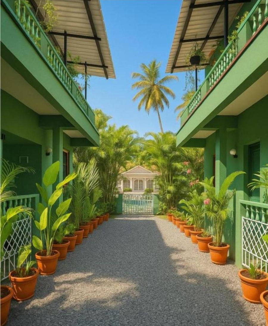 A gravel path between two green two-storey wings, lined with potted palms, leading to a white gate