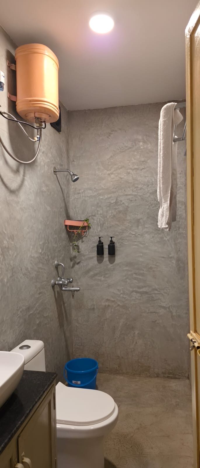 Shower area with textured grey walls, a water heater and wall-mounted soap dispensers