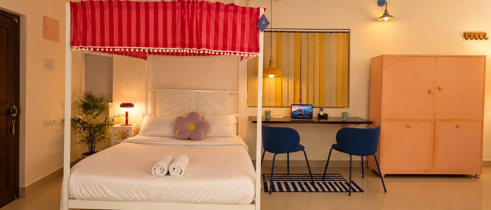 The studio: a white four-poster bed with a red striped canopy, a wall desk with two blue chairs, and a peach wardrobe