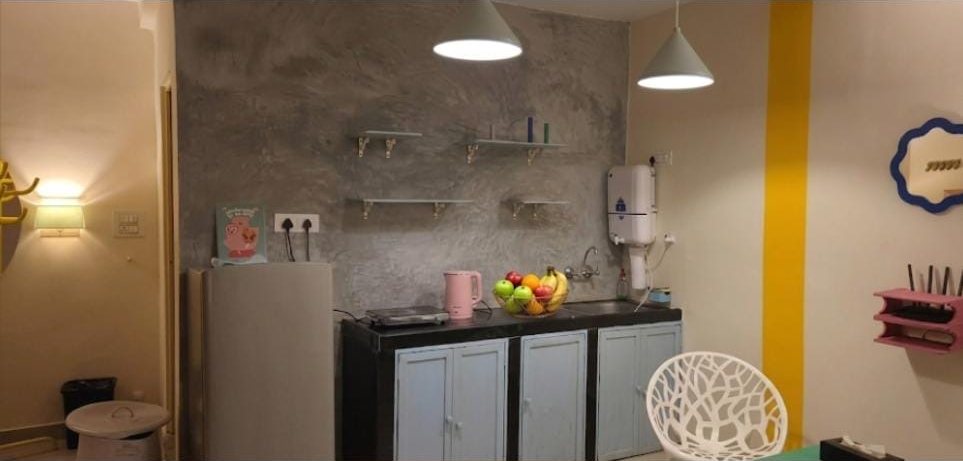 Kitchenette with a fridge, induction hob, kettle, sink, water purifier and open shelves against a grey textured wall