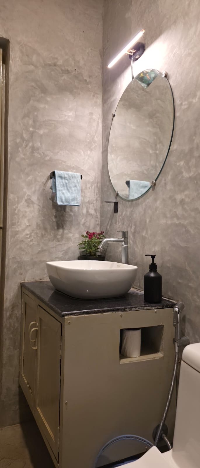 Bathroom vanity with a white vessel basin, a round mirror and a light bar on textured grey walls